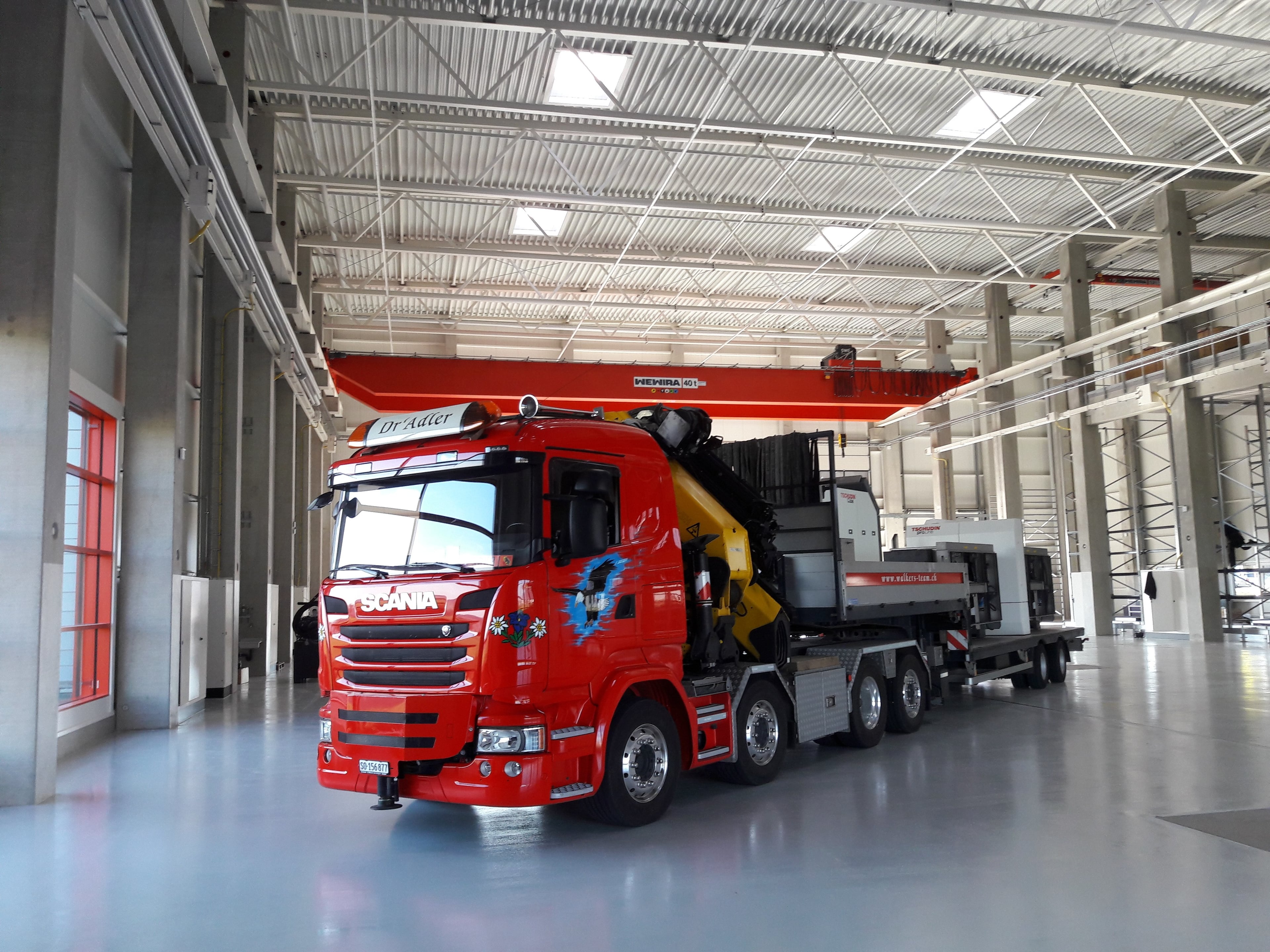 Red Scania truck with specialized industrial transport equipment in modern warehouse - Walker's Team industrial moving service