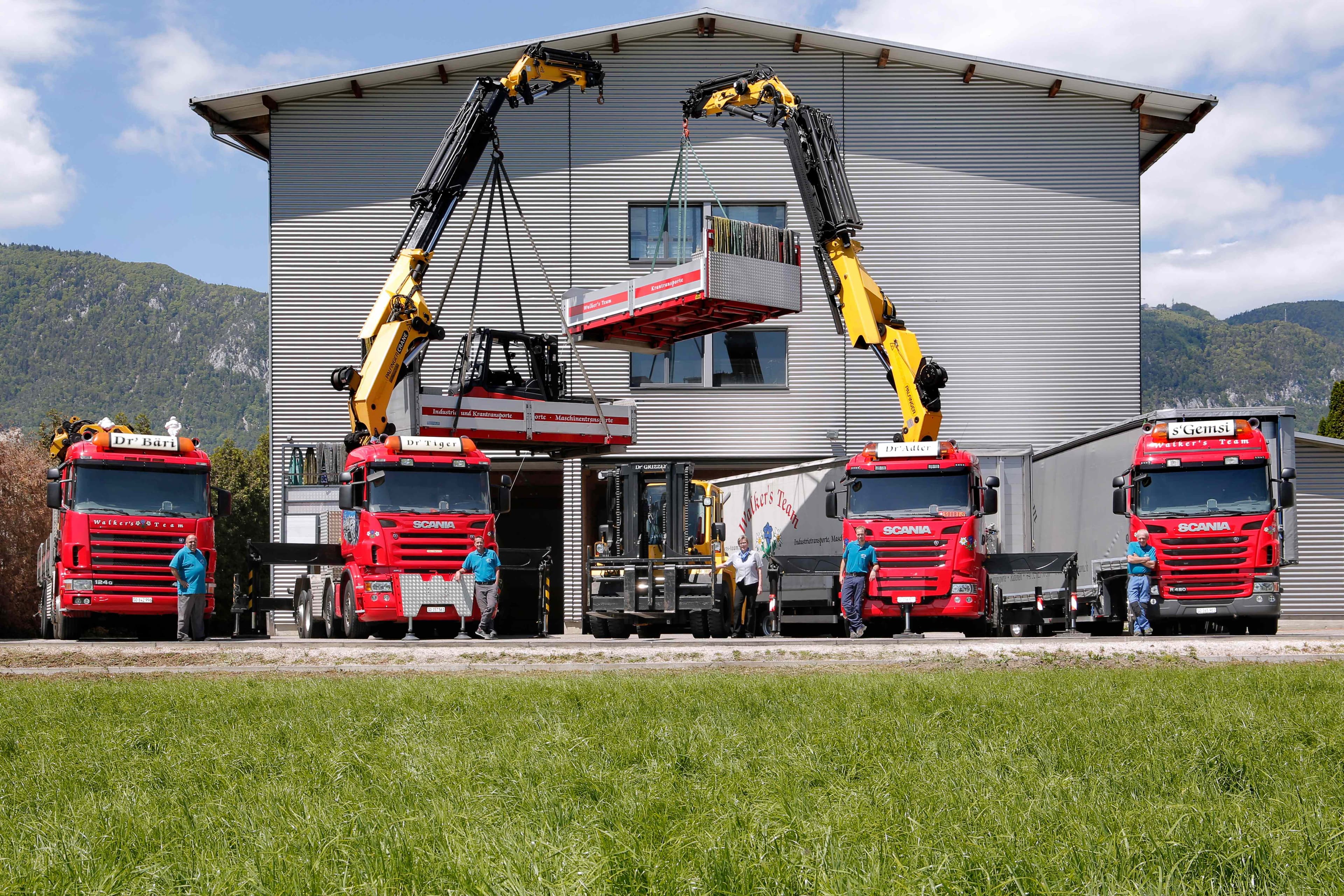 Multiple red Scania trucks working together in crane operation lifting modular building component